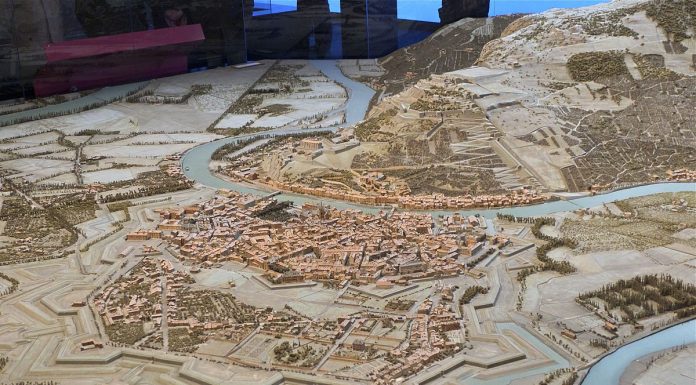 Vauban et les Plans-Reliefs A detailed scale model in the style of Vauban’s Plans-Reliefs depicts a historic city ringed by defensive walls and bastions, winding rivers and bridges; packed buildings fill its core, with hills, roads, fields, and trees beyond.