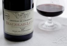 VIVA BEAUJOLAIS ! (Hymne joyeux) Gros plan sur une bouteille de vin étiquetée Château de Lavernette Beaujolais-Leynes 2007 à côté d'un verre de vin rouge sur une nappe blanche - une scène joyeuse célébrant le Beaujolais, avec des éléments décoratifs et les noms de Bertrand, Anke et Xavier de Boissieu.
