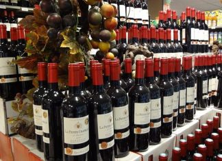 Best Vintage Years for French Wines Rows of red wine bottles labeled La Pierre Cachee, one of the best French wines, are neatly stacked on display in a store. Artificial grapevines with multicolored grapes and leaves hang above, while more vintage year bottles line the shelves behind.