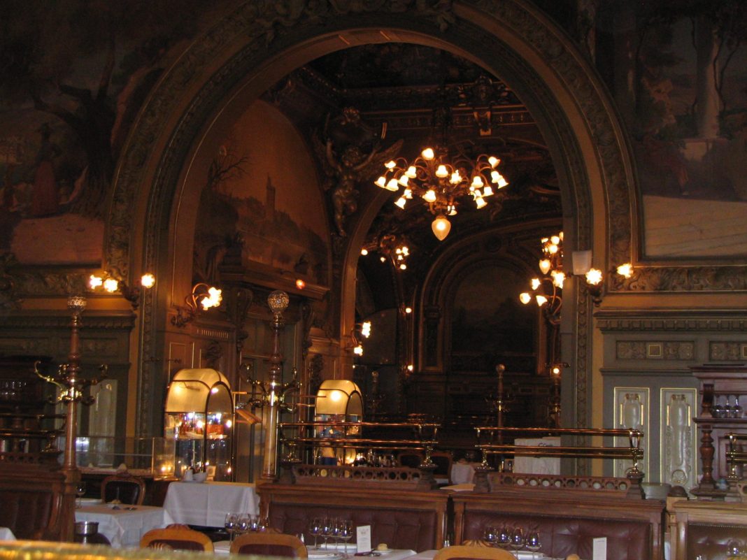 train-bleu-paris-08 L'intérieur du restaurant, orné de portes cintrées, de décorations dorées et de peintures classiques, évoque l'élégance de la France. L'éclairage chaleureux des lustres se reflète sur les surfaces en miroir et les tables dressées, créant une ambiance luxueuse et historique pour tout visiteur qui vient pour la première fois.