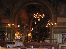 Ornate restaurant interior with arched doorways, golden decorations, and classical paintings evoke the elegance of France. Warm lighting from chandeliers reflects on mirrored surfaces and set tables, creating a luxurious, historic ambiance for any first time visitor.