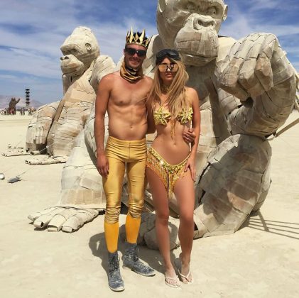A man and woman in gold costumes pose in front of large, sculpted gorilla figures on a desert playa under a blue sky—one of those BurningMan photos that capture the surreal, almost photos impossibles moments found at this iconic festival.