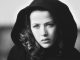 Les bonheurs de Sophie Marceau Black and white close-up of a young woman with wavy hair, her serious gaze and dark hooded coat echoing the poise of Sophie Marceau. The blurred background draws focus to her contemplative expression, inviting quiet bonheurs.