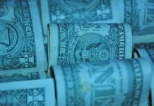 Convention Fiscale Franco-Américaine Several U.S. one-dollar bills are rolled up and stacked closely together, displaying intricate engravings and the word “ONE.” With a blue-green tint, the image evokes themes of fiscalité, reminiscent of Convention Fiscale Franco-Américaine discussions.