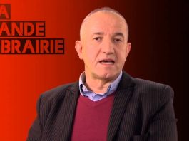 A middle-aged man in a striped dark suit jacket, light blue shirt, and burgundy sweater sits before a red and black gradient background. “LA GRANDE LIBRAIRIE” and “J'aime l'humain – Philippe Claudel” appear in bold red and black letters on the left.