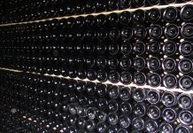 Acheter son vin sur Internet Rows of dark glass wine bottles are stacked horizontally in a cellar, their bottoms facing outward. Neat, parallel lines on shelves create a geometric pattern—ideal inspiration for those looking to acheter vin en ligne and expand their collection.