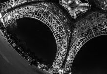 La musique française sur le marché américain A black-and-white, low-angle view of the Eiffel Tower at night, its illuminated iron lattice arches curving dramatically through a fisheye lens—like musique française echoing across Paris, capturing the city’s timeless allure for the marché américain.