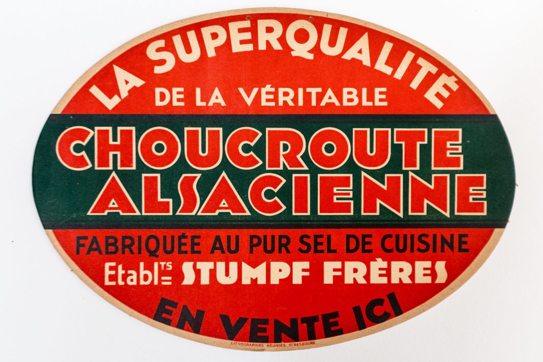 Carton_publicitaire_choucroute_alsacienne_Stumpf_Frères (1) An oval vintage sign in red, green, and beige reads La Superqualité de la véritable Choucroute Alsacienne, celebrating authentic Sauerkraut. Bold, decorative text dominates the design and highlights its artisanal quality.