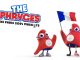 Paris 2024 Olympic Mascot The Phryges Two red, soft, triangular mascots called “The Phryges” stand together. One mascot holds a French flag and has a prosthetic leg. Both wear sneakers and Paris 2024 Olympic badges. “THE PHRYGES PARIS 2024 OLYMPIC MASCOTS” appears above them in bold text.