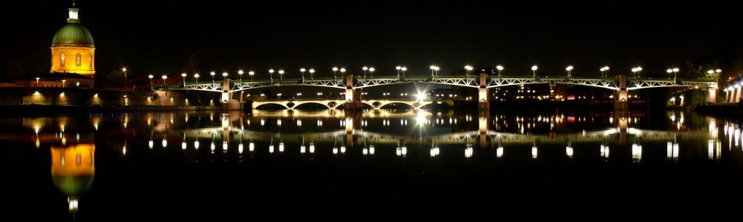 Toulouse Pont Saint-Pierre et Hôpital de La Grave The illuminated Pont Saint-Pierre bridge spanning the Garonne River at twilight with the iconic copper dome of the Hôpital de La Grave reflecting in the water.