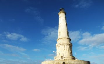 Le Phare de Corduan A white stone lighthouse nestled on a round three storey round base rises into a deep blue september sky.Tourists are mingling around the lighthouse and base which is accesible because of low tide.