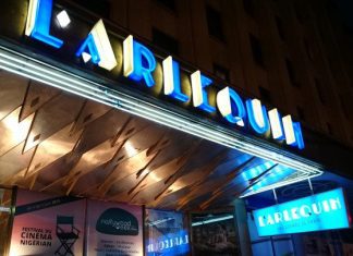 Enchanté Cinéma : Dévoilement des films français incontournables de 2022 et 2023 La photo montre l'entrée de L'Arlequin, un cinéma connu pour ses films français, avec son nom en lettres de néon bleu vif. La marquise brille au-dessus des affiches de films de 2022 2023, et un panneau bleu "L'Arlequin" est accroché près de l'extérieur chaleureusement éclairé.