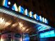 Enchanté Cinéma: Unveiling the Must See French Films of 2022 and 2023 Nighttime photo of the L’Arlequin cinema’s entrance. Its name glows in blue neon above the door. Posters for the 2023 Nigerian Cinema Festival, Nollywood Week, and French films are visible in the glass below. The building appears gold-toned.